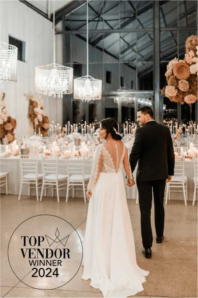 6 Newly married couple holding hands, walking into the candlelit Whispering Thorns glasshouse reception venue. The scene shows textured dried floral clouds, ornate crystal chandeliers, and long guest tables with white Chiavari chairs, overlaid with the 'Top Vendor Winner 2024' logo. Newly married couple holding hands, walking into the candlelit Whispering Thorns glasshouse reception venue. The scene shows textured dried floral clouds, ornate crystal chandeliers, and long guest tables with white Chiavari chairs, overlaid with the 'Top Vendor Winner 2024' logo.