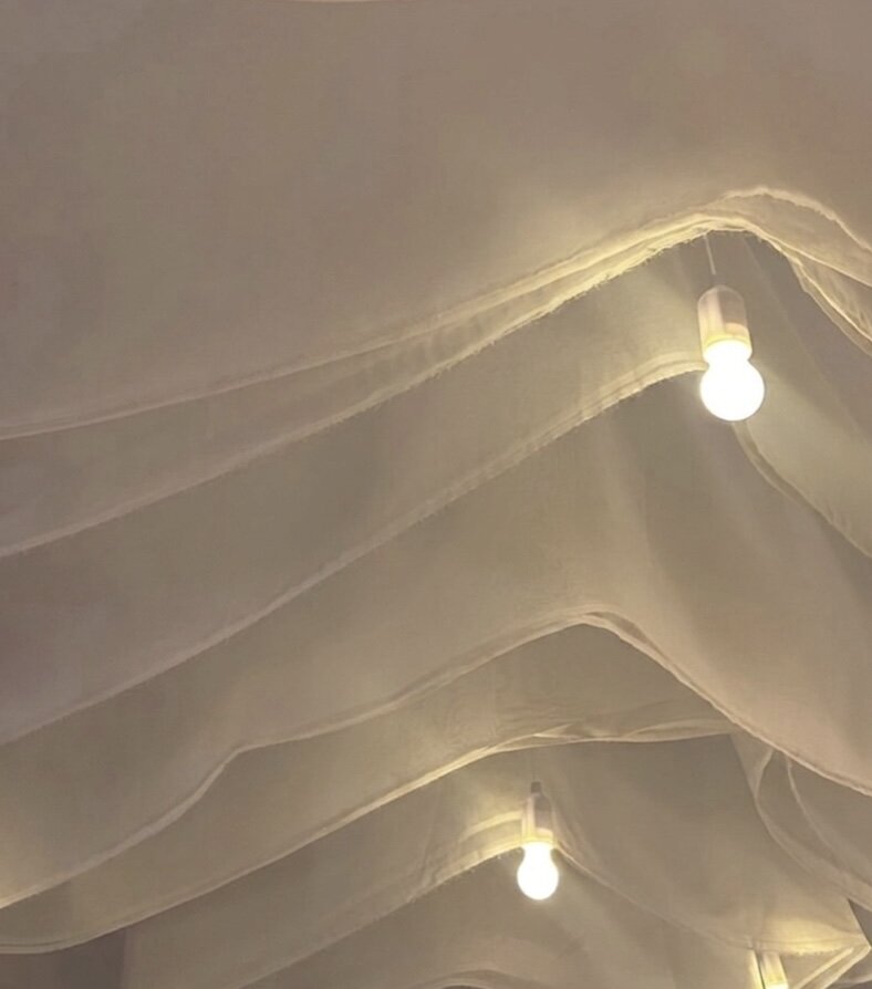 Whispering Thorns Kinetic Ceiling Drapery - 2026 Trend Close-up of pleated white luxury wedding drapery on a conservatory ceiling with warm pendant lighting at Whispering Thorns.